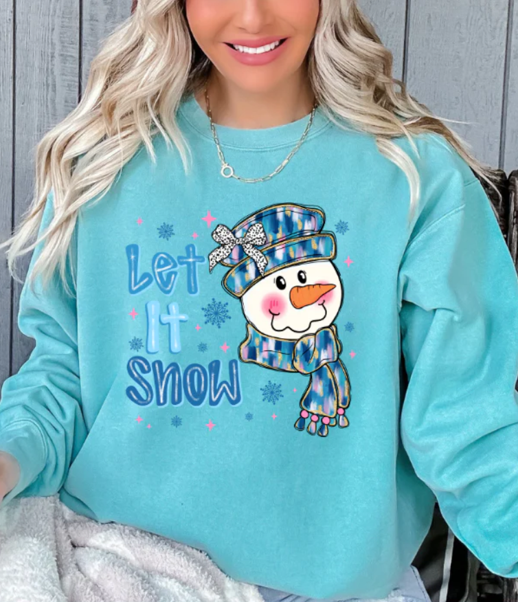 Turquoise winter sweatshirt with snowman wearing plaid hat and scarf and text “Let It Snow” surrounded by snowflakes and stars.