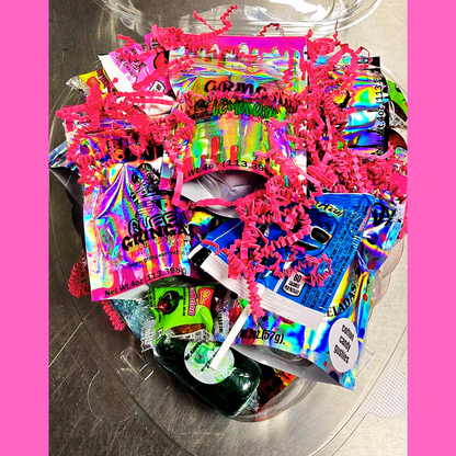 "Gringa’s Heart Candy Gift Box mockup featuring a clear heart-shaped container filled with assorted candies, pink shredded paper, and branded labels. Text reads 'Gringas Hearts – Candy That Says I Love You (or I Deserve This)' with a 'Limited Batches!' badge on a pink swirl background and Queen Gringa’s logo at the bottom."